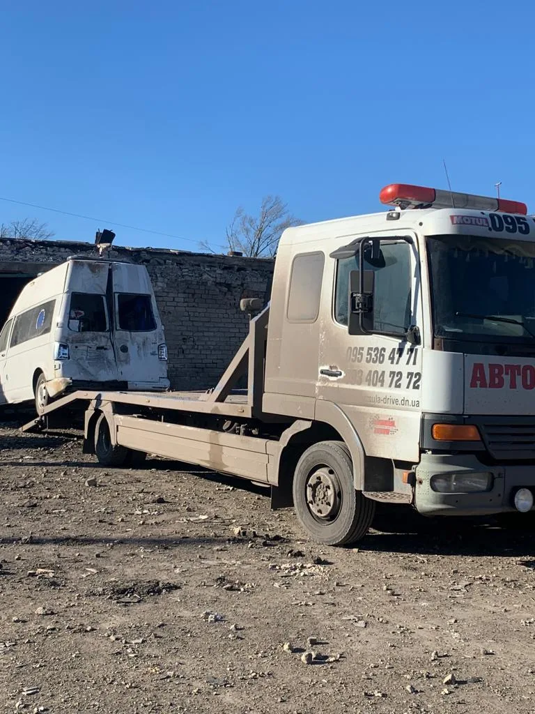 Bei einem Angriff auf Selydowe wurde der Krankenwagen zerstört. Dank Mechanikern vor Ort konnte er mit Teilen von anderen zerstörten Wagen repariert werden. Ein zerbeulter Krankenwagen wird von einem Lkw abgeschleppt.